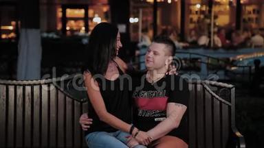 快乐的男人和女人在晚上的长凳上牵手聊天。